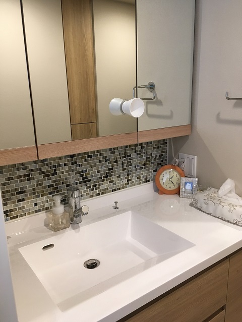 モザイクタイルを貼った壁が印象的な洗面室。大きな鏡や継ぎ目がなく掃除がしやすい洗面ボウル、ワンタッチでゴミ捨てができる収納扉など使い勝手を高める工夫が随所に見られる。